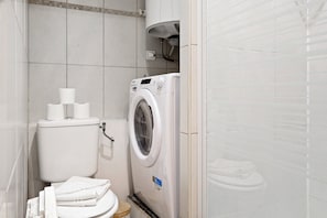 Une petite salle de bain comprenant des toilettes, un lave-linge et un porte-serviettes.
