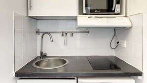Une cuisine de taille réduite avec des meubles blancs, un four à micro-ondes encastré, un évier et un réfrigérateur compact.