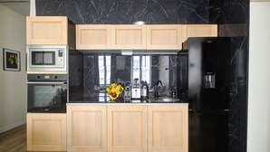 A modern kitchen with wooden cabinets, a black marble backsplash, a stainless steel refrigerator, and a microwave. - TBS 47 - Elegant apartment in Le Marais district (Paris)