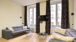 A modern living room with a grey sofa, a round coffee table, and a flat-screen TV mounted on the wall. - TBS 47 - Elegant apartment in Le Marais district (Paris)