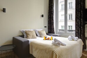 Ein Hotelzimmer mit einem Bett, einer grauen Couch, einem kleinen runden Tisch und einem Fenster mit Vorhängen.
