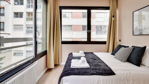 Et hotelværelse med en seng, et vindue med gardiner, en radiator og et billede i ramme på væggen.