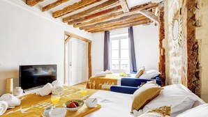 Habitación de hotel con techo de madera, cama con ropa blanca, televisor y bandeja de desayuno con cruasanes y jugo de naranja.