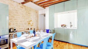 Comedor con pared de piedra, cocina con lavabo y sillas azules.