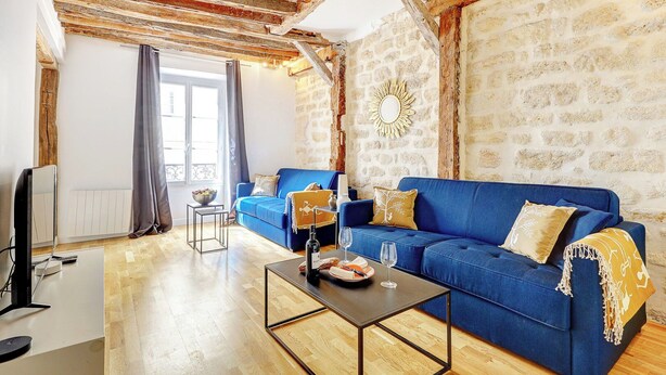 Un salón con un sofá azul, una mesa de centro, un televisor y una pared de piedra.