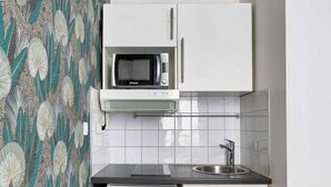 Una cocina compacta con armarios blancos, un microondas y un lavamanos.