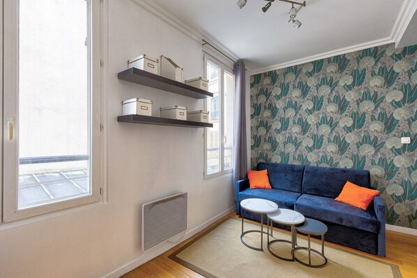 A living room with a blue sofa, two small round tables, and storage shelves on the wall. - TBS 176 - Cosy apartment in Paris (Paris)