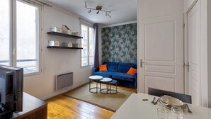 Una sala de estar con un sofá azul, una mesa redonda pequeña, un televisor y una puerta.