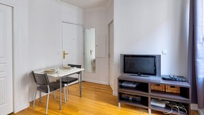 Habitación de hotel con una mesa de comedor, sillas, televisor y una pequeña unidad de entretenimiento.