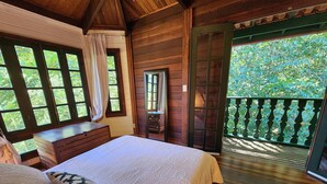 Un dormitorio de cabaña de madera con cama, cómoda y vistas al exterior a través de amplios ventanales.