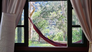 Una ventana con vistas a una hamaca y abundante follaje.