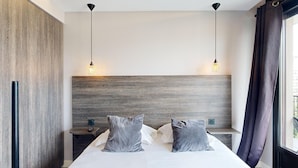 Une chambre d’hôtel moderne avec un grand lit, deux tables de chevet et une tête de lit en bois.