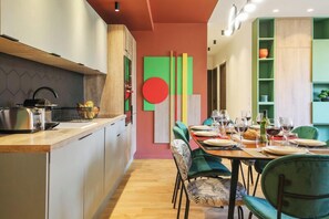 A modern kitchen with a wooden countertop, a sink, and a stove. There is a dining area with a table set for four, chairs, and a decorative wall with a large red circle. - TBS 88 - Elegant and modern apartment in Paris (Paris)