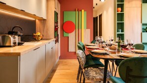 Een moderne keuken met een eethoek, houten kastjes en een kleurrijk abstract kunstwerk aan de muur.