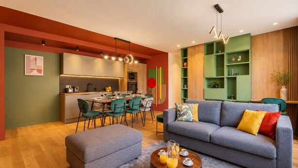 Een moderne woonkamer met een grijze bank, een salontafel met drankjes en een eethoek met stoelen en een tafel.
