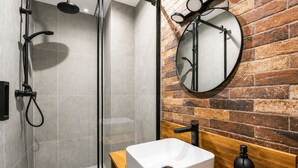 Een moderne badkamer met een douchecabine van glas, een wit wastafeltje en een houten badkamerkast.