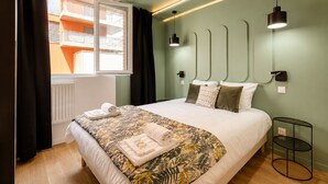 A hotel room with a bed, a window with curtains, a bedside table, and a wall-mounted light fixture. - TBS 88 - Elegant and modern apartment in Paris (Paris)