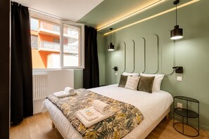 A hotel room with a bed, a window with curtains, a bedside table, and a wall-mounted light fixture. - TBS 88 - Elegant and modern apartment in Paris (Paris)