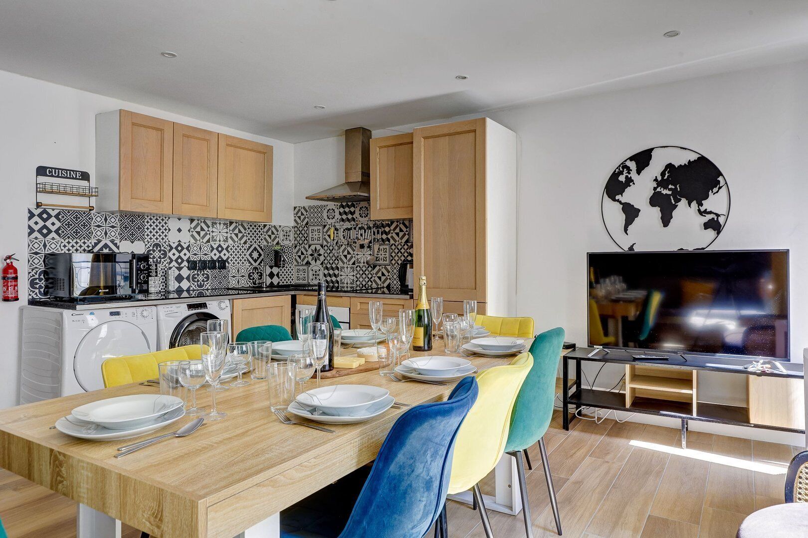 A modern kitchen with wooden cabinets, a tiled backsplash, and a dining area with a wooden table set for a meal.