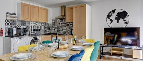 A modern kitchen with wooden cabinets, a tiled backsplash, and a dining area with a wooden table set for a meal.