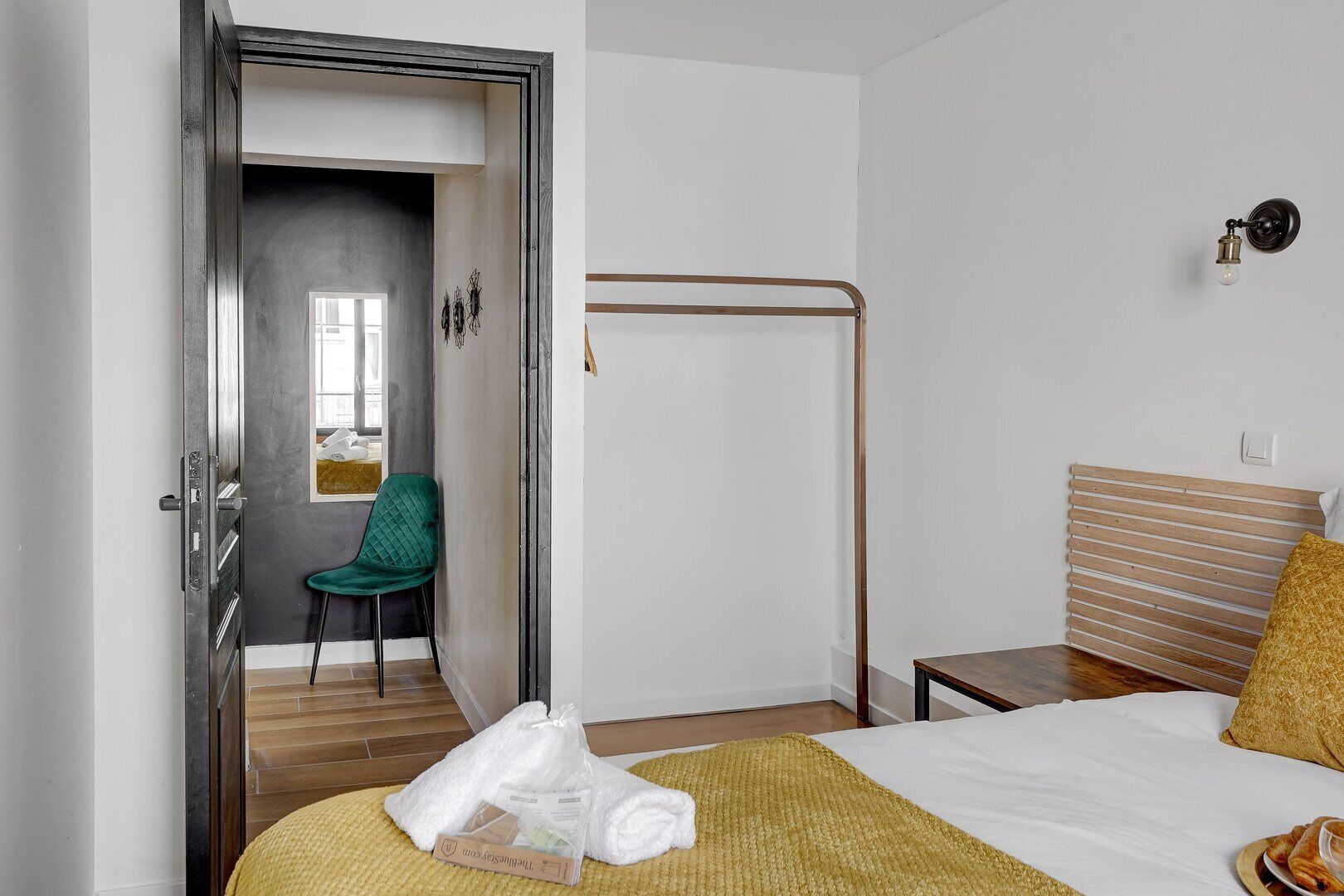 A hotel room with a bed, a chair, a towel, and a small table.