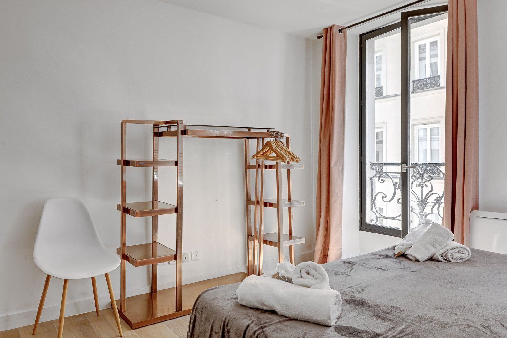 Ein Schlafzimmer mit einem Bett, einem Holzschrank, einem weißen Stuhl und einem Fenster mit Vorhängen.