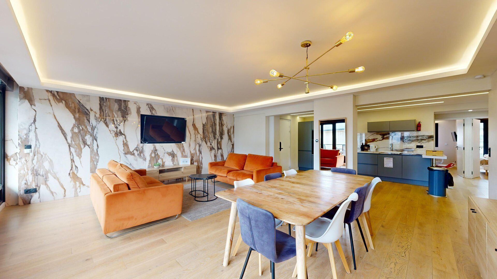 Una sala de estar moderna con pared de mármol, sofá naranja, mesa de comedor de madera y una cocina al fondo.