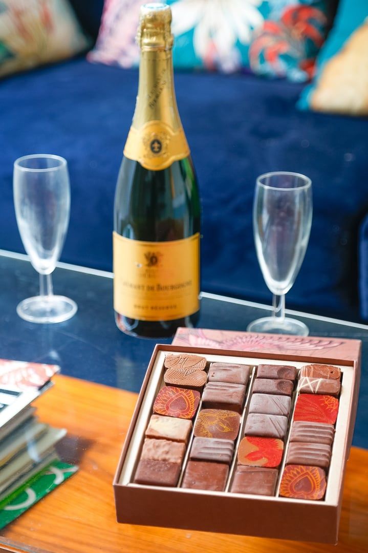 A bottle of champagne, two empty glasses, and a box of chocolates on a table.