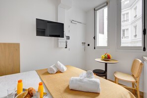 Relax in a serene space with a neatly made bed, flat-screen TV, and a small table with fresh fruit.