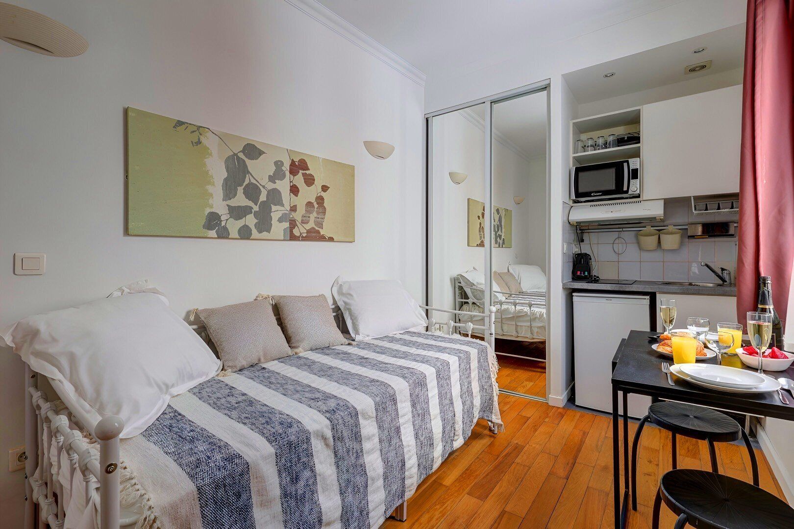 Une pièce compacte comprenant un lit, une table à manger avec des chaises, un coin cuisine et une porte coulissante donnant accès à une salle de bain.