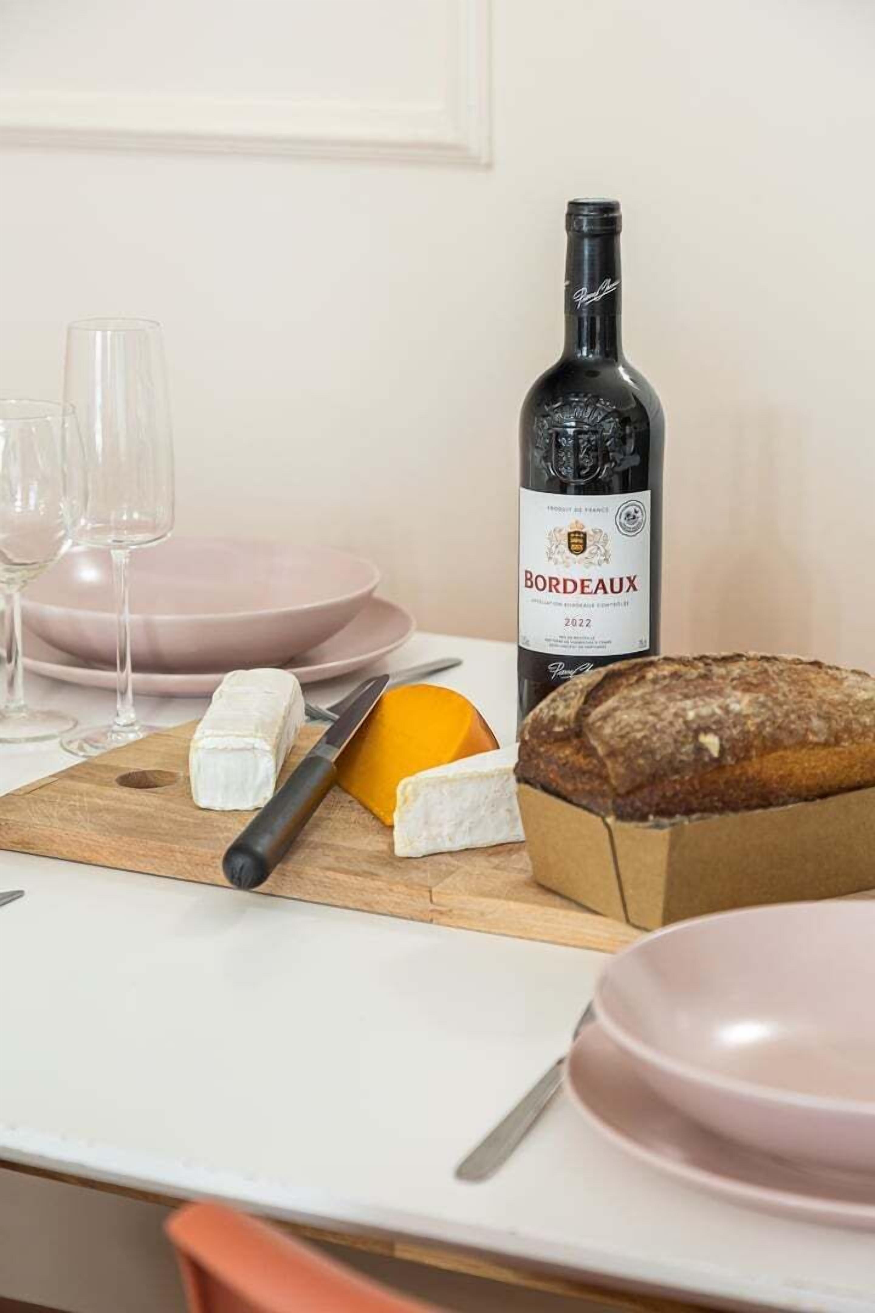Ein Tisch mit einer Flasche Bordeauxwein, einem Brotlaib, einem Käse und einem Messer.