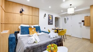 A modern hotel room with a bed, bedside table, and a dining area with a table and chairs.