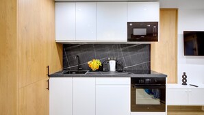 A modern kitchen with white cabinets, a black countertop, a built-in oven, and a microwave.