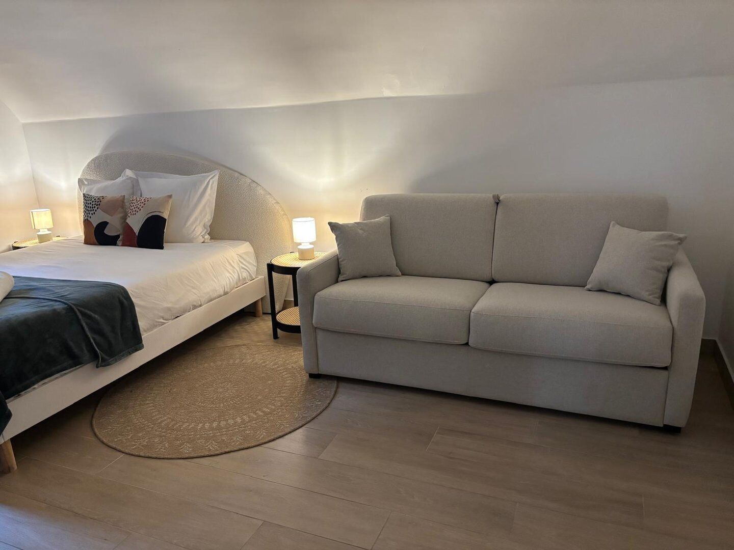 Un dormitorio con cama, sofá, mesita de noche con lámpara y una pequeña alfombra.
