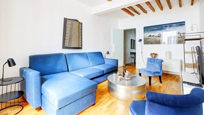 A living room with a blue sofa, a round coffee table, and a blue armchair. There is a painting on the wall and a wooden ceiling. - TheBlueStay 284 - Charming Apartment - Le Marais (Paris)
