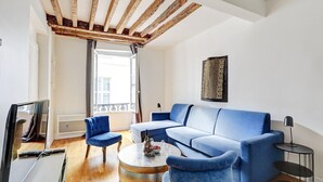 A modern living room with a blue sofa, two matching armchairs, a round coffee table, and a TV on a stand. - TheBlueStay 284 - Charming Apartment - Le Marais (Paris)