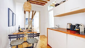 A modern kitchen with wooden beams, a dining area with a table set for two, and a view of the outdoors. - TheBlueStay 284 - Charming Apartment - Le Marais (Paris)