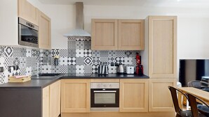 A modern kitchen with wooden cabinets, a built-in oven, a microwave, and patterned backsplash tiles. - TBS 161 - Spacious apartment in the heart of Paris (Paris)