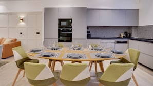 A modern kitchen with built-in appliances, a dining area with a round table set for six, and a living area with a sofa and armchairs. - TBS 61 - Pretty suite near Roland-Garros stadium (Paris 16 Passy)