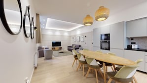 A modern kitchen with built-in appliances, a dining area with a wooden table and chairs, and a living area with a sofa and TV. - TBS 61 - Pretty suite near Roland-Garros stadium (Paris 16 Passy)