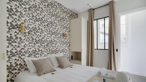 A hotel room with a geometric-patterned wall, a bed with white linens, and a window with curtains. - TBS 61 - Pretty suite near Roland-Garros stadium (Paris 16 Passy)