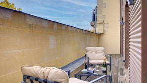 Ein Balkon mit zwei beigefarbenen Liegestühlen, einem kleinen Tisch mit einer Champagnerflasche und einem Glas. Der Balkon hat eine gelbe Wand und ein Metallgeländer.