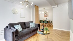 A modern living room with a dark grey sofa, a glass coffee table, and a dining area with a wooden table and chairs.