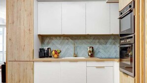 A modern kitchen with white cabinets, a herringbone-patterned backsplash, and a wooden floor.
