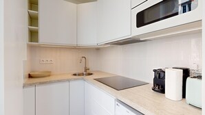 A modern kitchen with white cabinetry, a stainless steel sink, a black countertop, a microwave, a toaster, and a dish drying rack. - TBS 285 - Elegant and modern apartment in Paris (Paris)