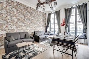 A modern living room with a brick wall, a sofa, a coffee table, and a dining area with a table set for two. - 17 Suite Wiz – Charming Apt 8 guest - Paris 1 (Paris)