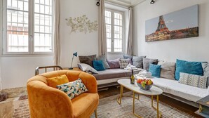 En stue med sofa, lænestol og sofabord, med et maleri af Eiffeltårnet.