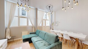 Un salon moderne avec un canapé de couleur turquoise, une table à manger avec des chaises et un lustre aux ampoules apparentes.