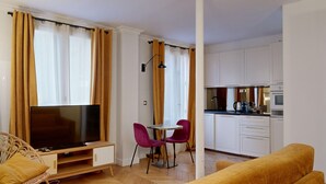 Un espacio habitable compacto con televisor, una mesa de comedor con sillas, un sofá y una kitchenette.
