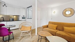 Una cocina moderna con armarios blancos, un comedor con una mesa redonda y sillas, y una sala de estar con un sofá y una mesita de centro redonda.